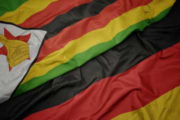 waving colorful flag of germany and national flag of zimbabwe.