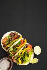 Corn tortillas with beef and vegetables, beer and lime on a black surface, top view. Mexican...