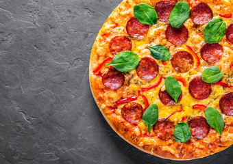Pepperoni Pizza with Mozzarella cheese, salami, pepper, Spices and Fresh spinach. Italian pizza on Dark grey black slate background