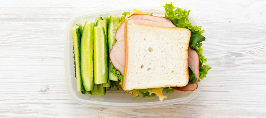 Lunch box with sandwich and vegetables on a white wooden surface, top view. From above, overhead.