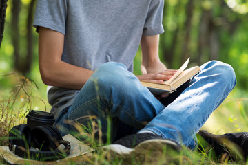 Young man student reading a book and preparing for exams sitting on the grass in the Park.