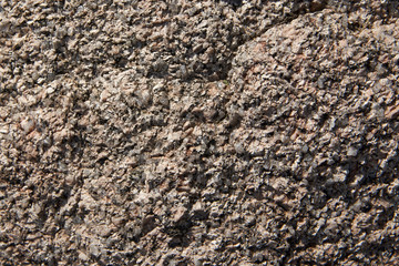 A fragment of the surface of a stone made of granite with a large grainy structure. Background, texture