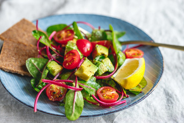 Vegetarian healthy salad is made from swiss chard leaves, cherry tomatoes, avocado, lemon juice and olive oil into a ceramic portion plate.