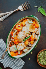 Top view on seasonal autumn low calorie recipe from baked turkey medallions with pumpkin, onion, champignons and sage in a ceramic dish.