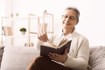 Senior man in glasses enjoying good book with smile