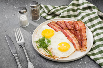 Scrambled eggs with bacon in a white plate on a grey table. Breakfast
