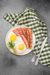 Scrambled eggs with bacon in a white plate on a grey table. Breakfast