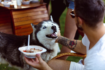 Young man and his dog at barbecue dinner on sunset time. Having meal outdoor in a forest glade or...