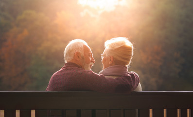 Senior couple sitting on bench in autumn park - obrazy, fototapety, plakaty