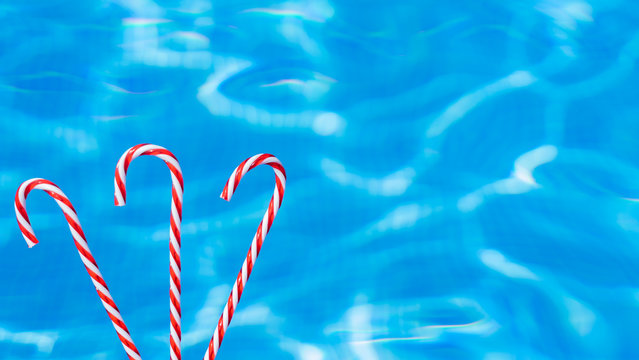 red candy cane on blue water background. New Year and Christmas on pool. Christmas moody background. Copy space. New Year in summer.