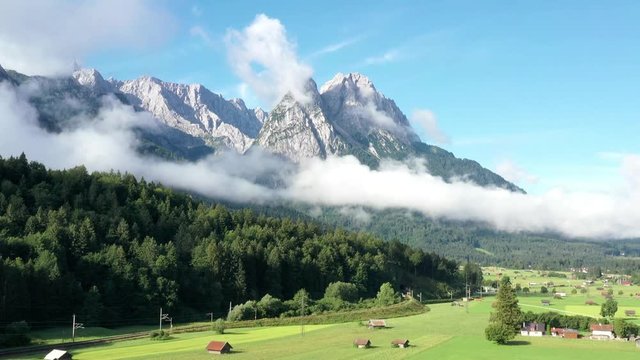 The Zugspitze, the highest mountain of Germany in the south of Bavaria at the border to Austria, is filmed from the air, with a meadow in the foreground.