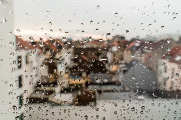 Fotobehang Raindrops on the glass. Outside the window, a city view of the roofs. The concept of a sad mood, autumn. White, beige, brown colors. © Елизавета Завьялова