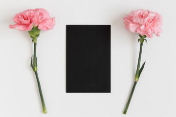 Top view of a black card mockup with pink carnations on a white table.