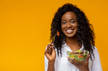 Happy african american woman eating vegetable salad