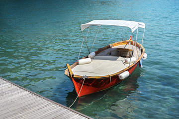 Obraz premium Red wooden boat with lying surface and sun canopy on the jetty in the turquoise water of the Mediterranean sea, copy space