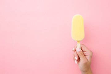 Young woman hand holding ice cream with white chocolate glaze on pastel pink background. Closeup....