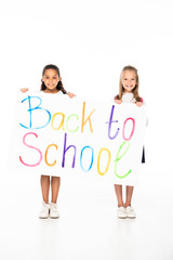 two cheerful multicultural schoolgirls holding placard with back to school inscription on white background