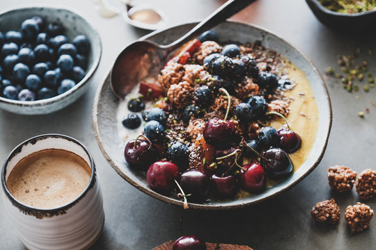 Healthy vegan breakfast set. Quinoa oat granola coconut yogurt bowl with fruit, seeds, nuts, berries and coffee over grey concrete background, selective focus. Vegetarian, dieting food concept