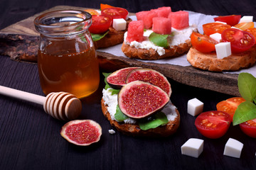 Bruschetta with figs, soft cheese, arugula and honey on black table