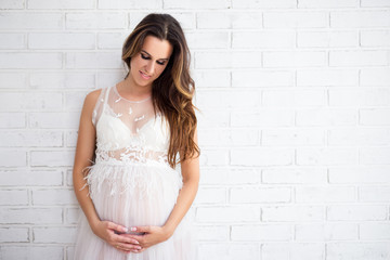 portrait of beautiful pregnant woman in white dress and copy space over white brick wall