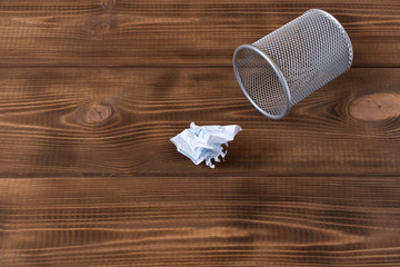 Crumpled sheet of paper and metal basket. On a wooden background.