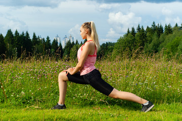 young woman doing exercises stretching in a meadow outside the city