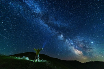 Fantastic starry night with galaxy Milky Way with a tourist and a tent on the mountain range in the...