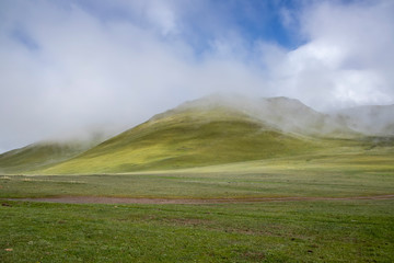 The road on the green field. Hills with descending fog. Kyrgyzstan