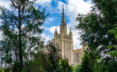 Naklejka premium View from territory of Moscow zoo on residential building among foliage of trees. High-rise building on Kudrinskaya Square one of seven Stalinist high-rise buildings . Moscow, Russia, June, 2019. 