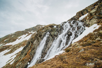 Fototapeta na wymiar Alpine waterfall in mountain. Alps. Snow. Poster Image. Trekking.