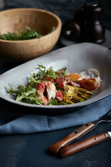 Salad with crab and avocado on a dark background. Arugula salad leaves seasoned with sauce on white wine with crab meat and grilled avocado in soft focus.