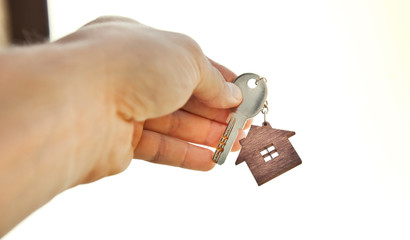 Obraz premium The mental key from door with wooden trinket in shape of house in man's hand in front of sky