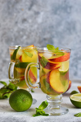 Cold summer drink with peach, lime and mint on a concrete background.