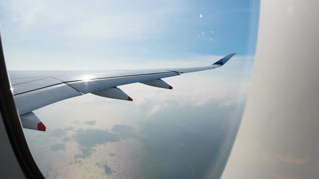 Hyperlapse view trough plane window of jet wing turning around above the sea and flying through white clouds 