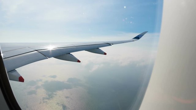 Zooming in hyperlapse view trough plane window of jet wing turning around above the sea and flying through white clouds 