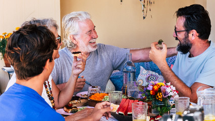 Happy and smiling multi-generation family. A senior couple with son and grandson enjoying brunch or meal together. Sunlight on the terrace field