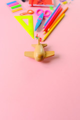 wooden toy airplane carries a various stationery on light pink background.
