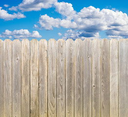 Whitewashed rustic wood privacy fence with blue sky and clouds