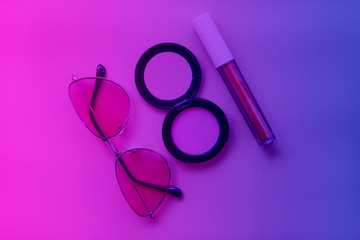 Lip gloss, rouge and sunglasses are toned on trendy neon colors – pink, violet and blue. Makeup and fashion concept. Flat lay 