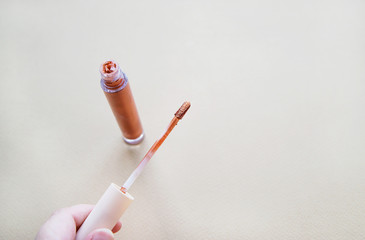 Bronze lip gloss in a hand. Autumn beauty and makeup concept. Warm colors