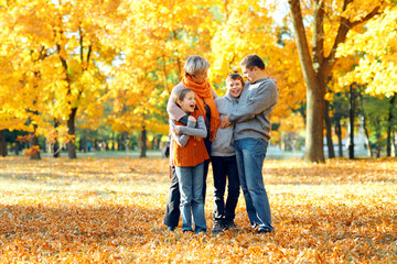Happy family posing, playing and having fun in autumn city park. Children and parents together having a nice day. Bright sunlight and yellow leaves on trees, fall season.