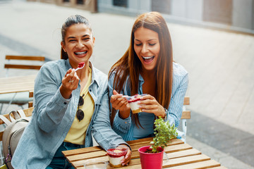Two female friends having fun eating cheesecake outdoors