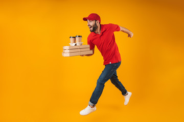 Portrait of young delivery man in red uniform running with pizza boxes and takeaway coffee