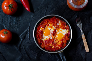 Shakshouka or shakshuka, eggs in a sauce of tomatoes and peppers, top view, dark background, copy space for your text