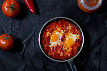 Shakshouka or shakshuka, eggs in a sauce of tomatoes and peppers, top view, dark background, copy space for your text