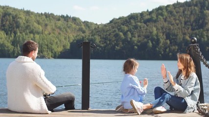 Happy family with daughter spend time fishing at the beautiful lake.