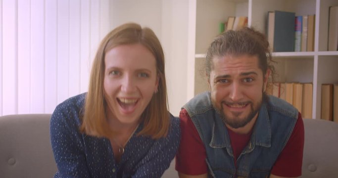 Hipster young couple plays videogame using joysticks being absorbed and the guy fails and gets sad.