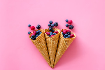 Summer breakfast with fresh berries in waffle cones on pink background top view