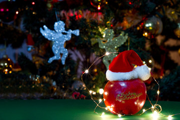 an apple with a christmas hat with a sticker saying merry christmas in german under a christmas tree