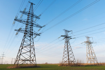 Fototapeta premium High voltage lines and power pylons and a green agricultural landscape on a sunny day.